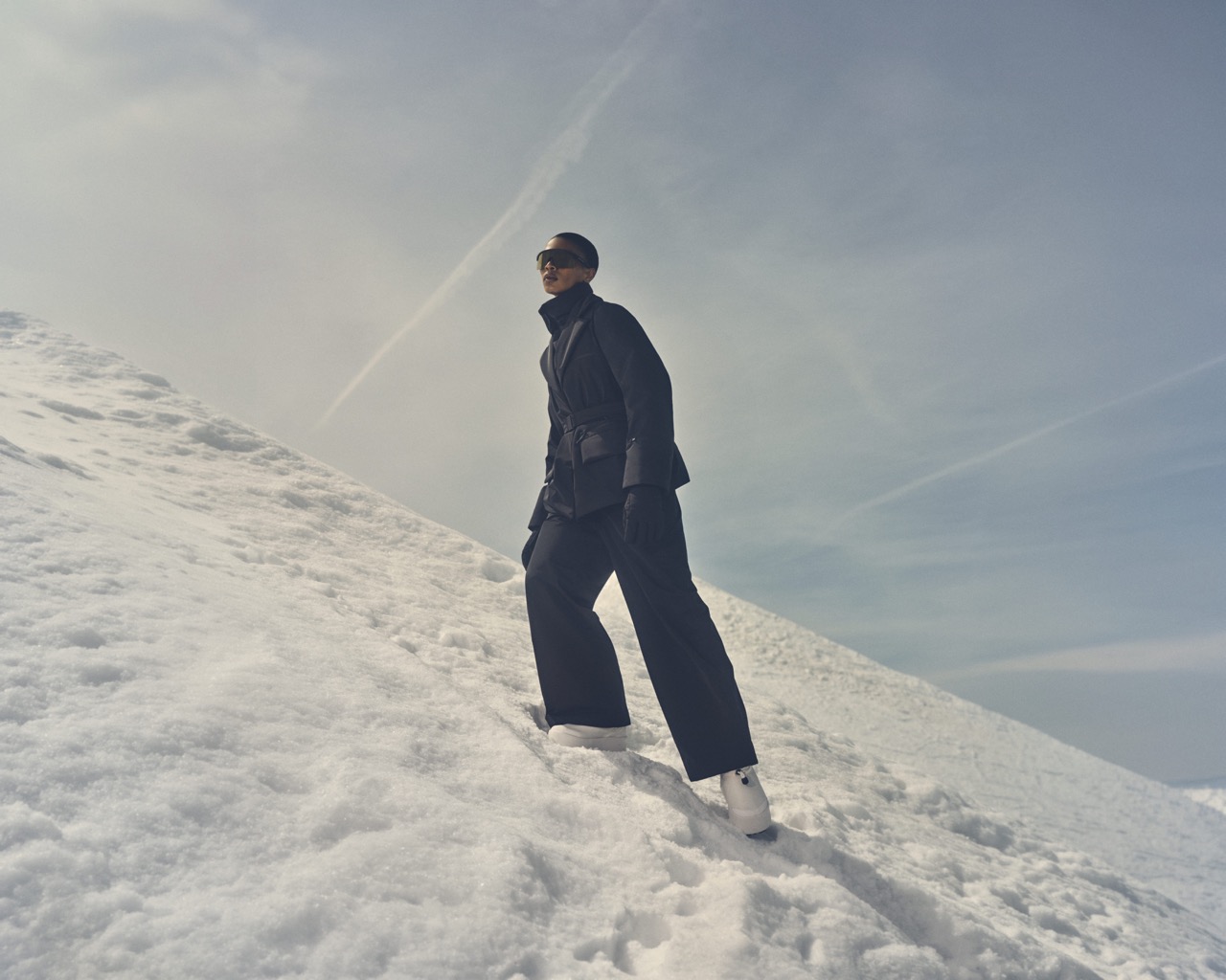 Model in a navy ski suit walking up a snowy ridge