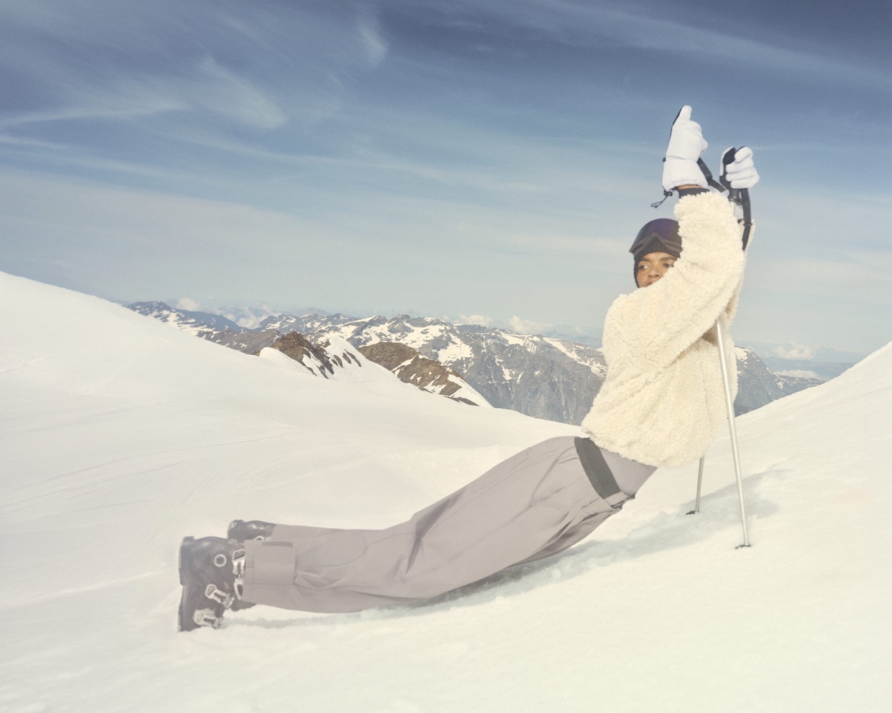 Model in a cream puffer jacket and muted purple ski trousers on a snowy slope
